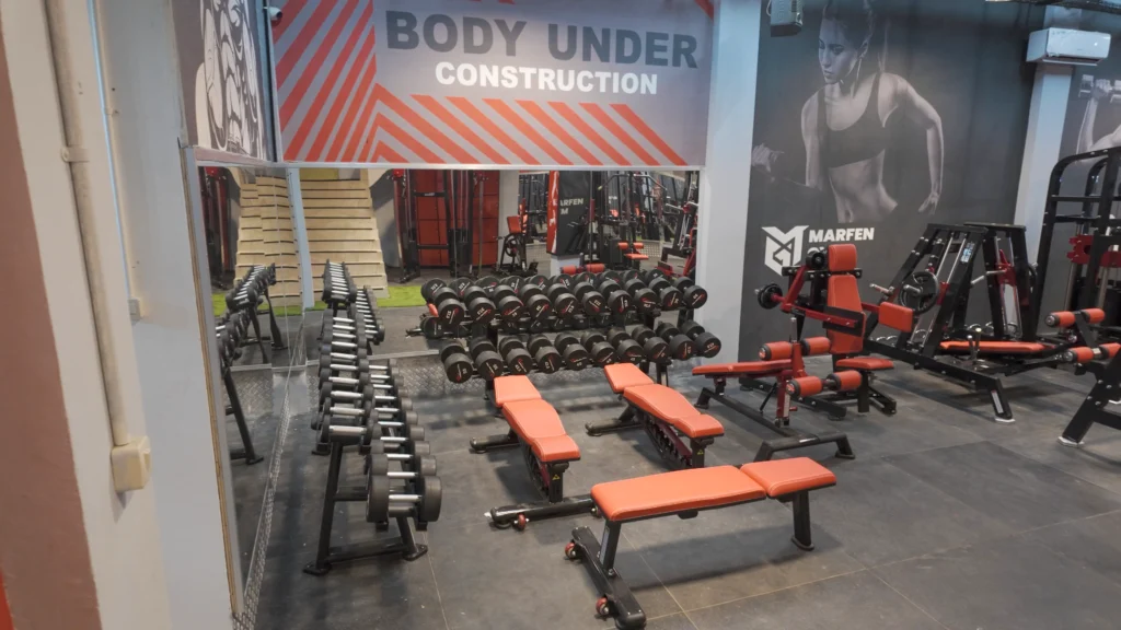 Penataan rak dumbbell dan bangku latihan di depan cermin besar untuk area gym terbatas.