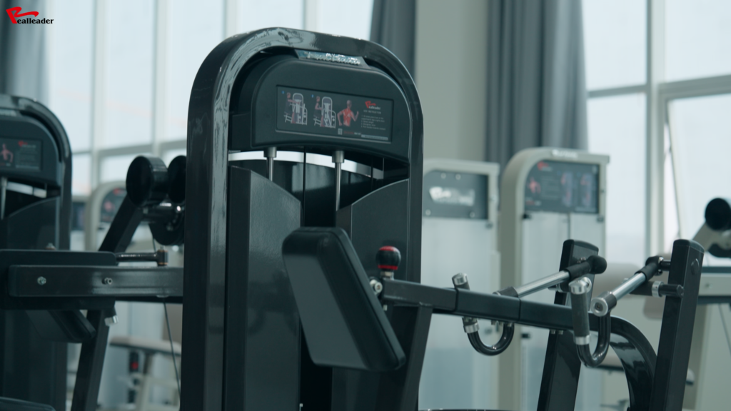 Gambar close-up dari mesin gym untuk duduk dengan diagram instruksional yang ditampilkan, ditempatkan di fasilitas kebugaran yang terang dan modern.